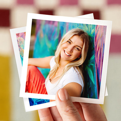 Hand holding a 4x4 photo print of a graduate sitting up against a colorfully painted wall outside. The print has a white border.