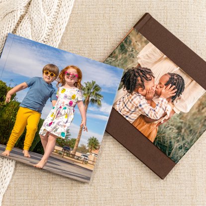 Two closed photo books lying on a blanket both featuring photos of a brother and sister on their front covers.