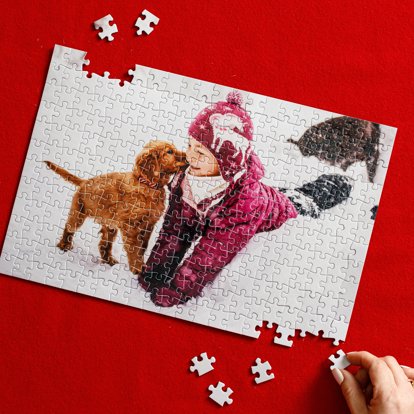 A photo puzzle being assembled that features a photo of a child playing outside in the snow with a small pet dog.