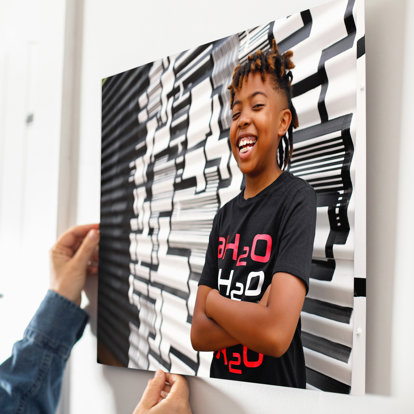 A 20x30" Metal Print being hung on a wall featuring senior photos of a smiling young man. 