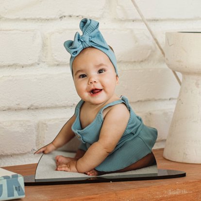 A statuette photo cut out of a baby wearing a blue ribbon and dress on a table. 