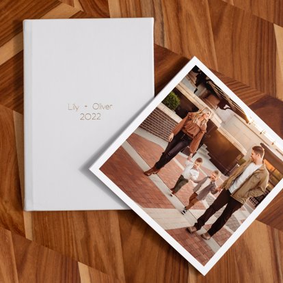 A signature leather photo album with a polar leather cover and gold debossing next to a softcover photo book with a photo of a family on the cover. 