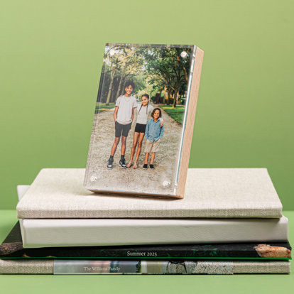 A birch photo block with magnetic frame displayed on a stack of photo books featuring a photo of three young siblings outside. 