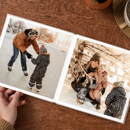 A hand flipping through an open photo book that features images of a family playing outdoors in the snow.