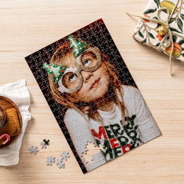 A photo puzzle almost fully assembled on a table featuring a photo of a child wearing holiday-themed glasses and a shirt that reads "Merry Merry Merry."