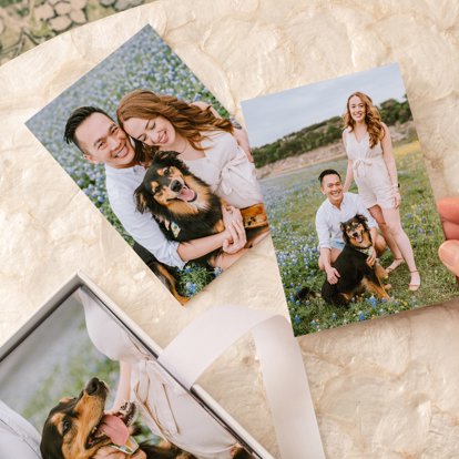 Two 4x6 photo prints lying on a table featuring a young couple with their dog in a field of wildflowers. 