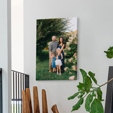 A canvas print hanging on the wall featuring a couple and their two young daughters standing outside in front of a large hydrangea plant.