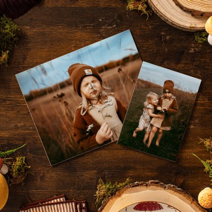 Two photo prints sitting on a wooden table next to fall decorations and featuring images of two young children.