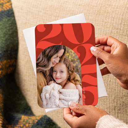 A hand holding a New Year Card featuring a family photo over a red background with the numbers "2025" along the right side of the design.