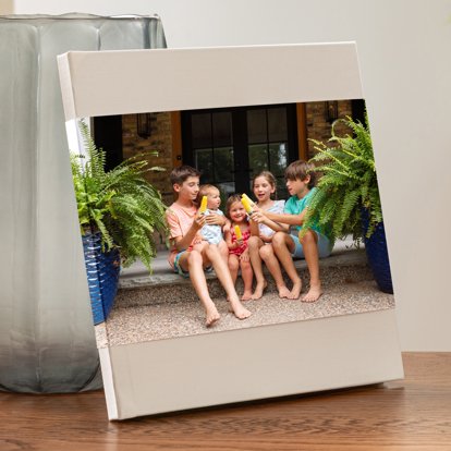 A hardcover photo book on a living room table with a tan linen cover and skinny photo dust jacket featuring an image of five children eating popsicles.