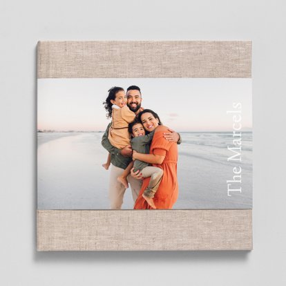 A closed photo book with a sand colored linen cover and a skinny dustjacket featuring a photo of a family on the beach.