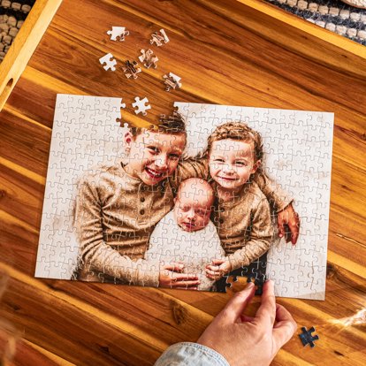 A close-up view of a hand assembling a photo puzzle from Mpix on a wooden surface.