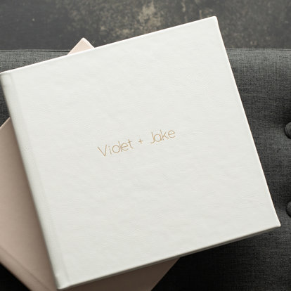 Two engagement albums with light leather covers laid out on a table. 