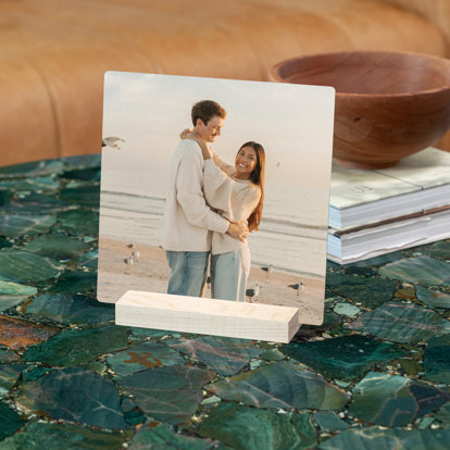 A tabletop metal print of a young couple on the beach. The print is upright in a maple wood stand displayed on a coffee table.
