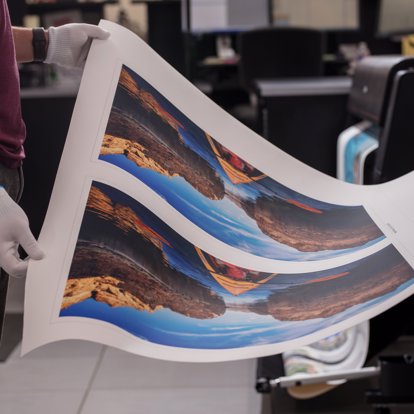 a worker removing a panoramic print from a printing machine to be inspected for quality.