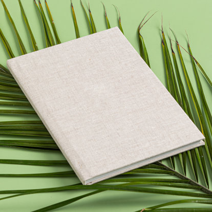 A closed 8x12 photo book with a sand color linen cover lying on a bed of palms