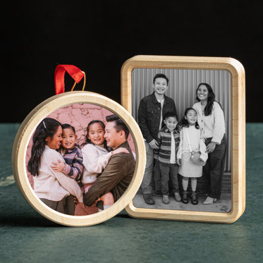Two framed photo ornaments displayed on a counter featuring photos from a family portrait session. The circle shaped ornament shows the hook and red ribbon used to hang the ornaments. 