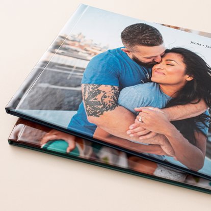Economy photo books from Mpix stacked on top of each other on a neutral background, the top book has a matte custom image cover of a couple embracing on a rooftop. 
