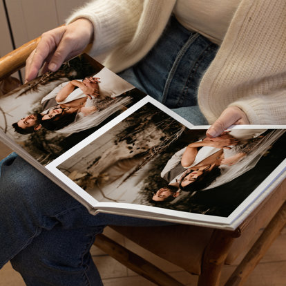 A hardcover wedding book with a sand linen cover lying open on a woman's lap featuring wedding photos of a bride and groom.