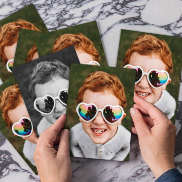 Photo print featuring an up-close shot of a boy wearing heart shaped sunglasses smiling and looking up at the camera.