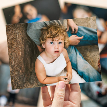 Close-up view of a 4x6 print featuring a toddler girl sitting on the ground in white overalls.